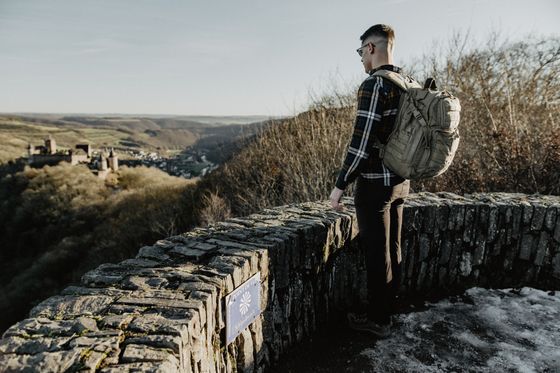 A man with a backpack stands on a stone observation platform and looks at a castle.