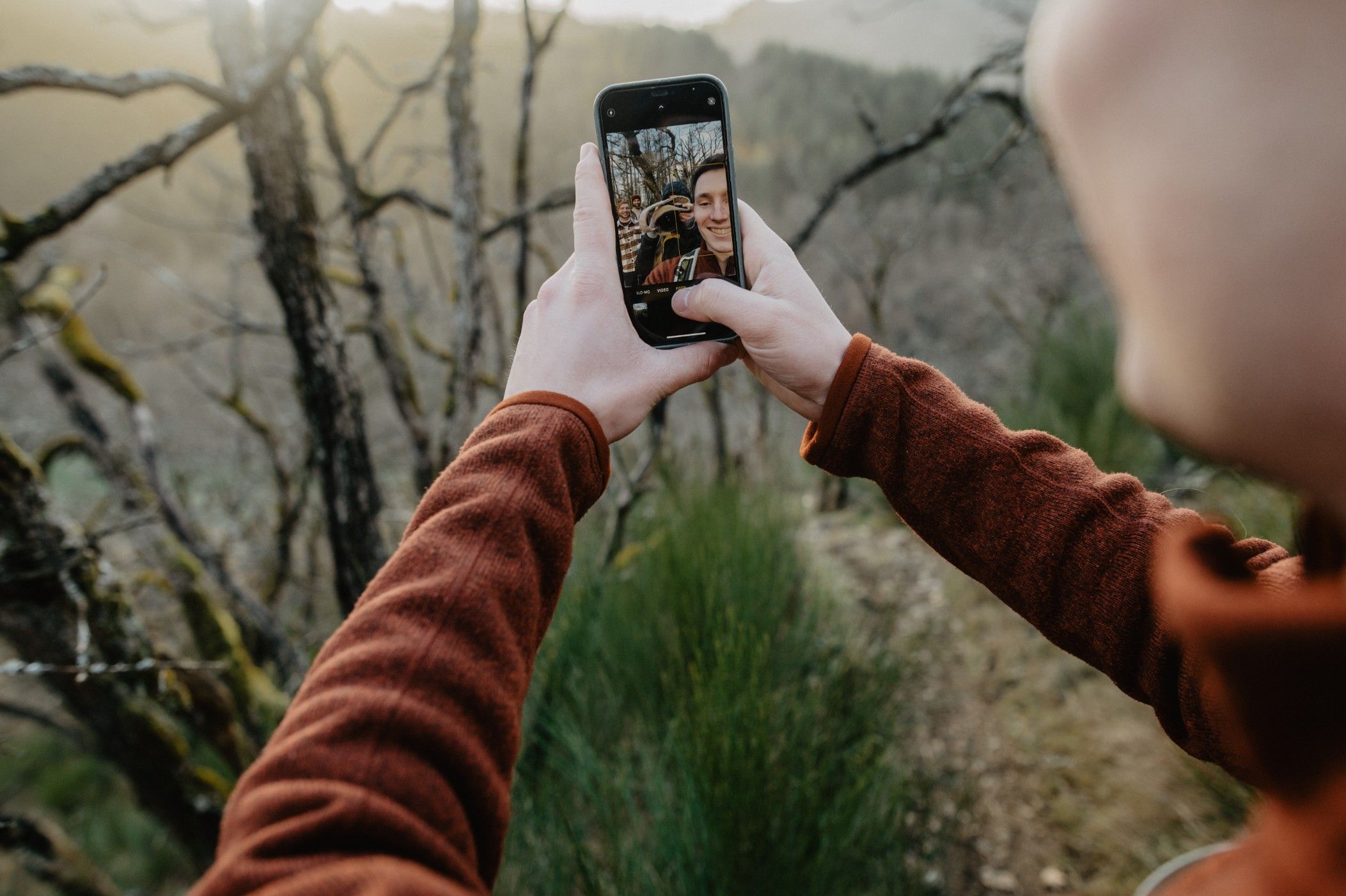 A man takes a photo of himself while hiking and laughs into the camera