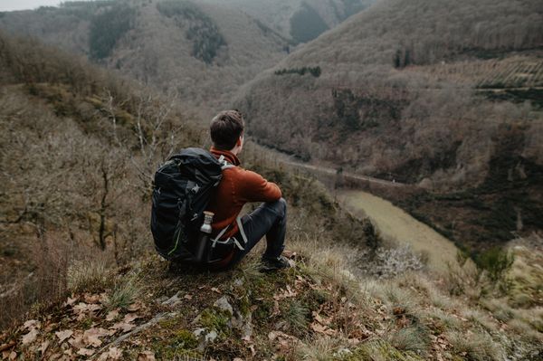 Ein Mann sitzt auf einem Hügel mit toller Aussicht und schaut in den Wald.