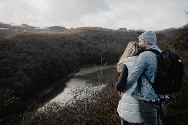 A couple embraces while standing at a viewpoint overlooking the river and the forest.