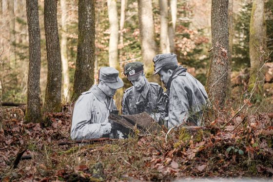 Un paysage forestier avec des figures grandeur nature en noir et blanc représentant des soldats qui regardent ensemble un livre.