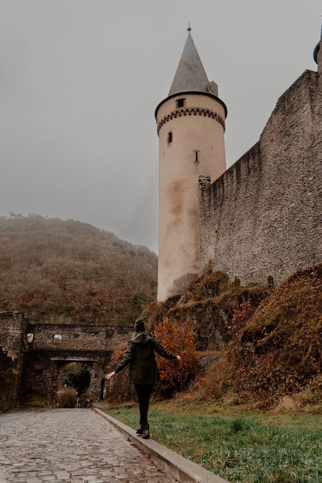 A woman balances on a curb, with a castle tower in the background on a foggy, gray day.