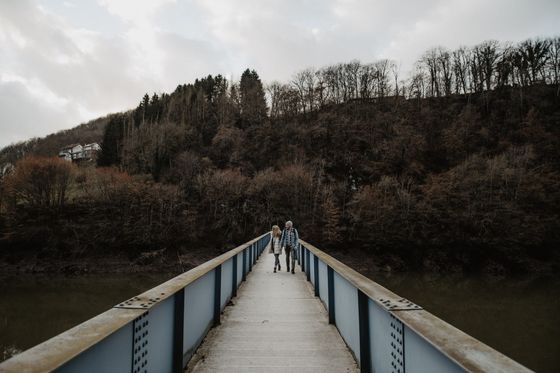 Un couple se promène sur un pont piétonnier avec une forêt en arrière-plan.