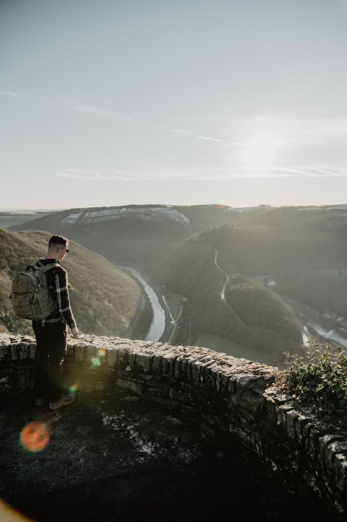 Ein Mann steht mit Rucksack auf einer Aussichtsplattform aus Stein und schaut ins Tal.